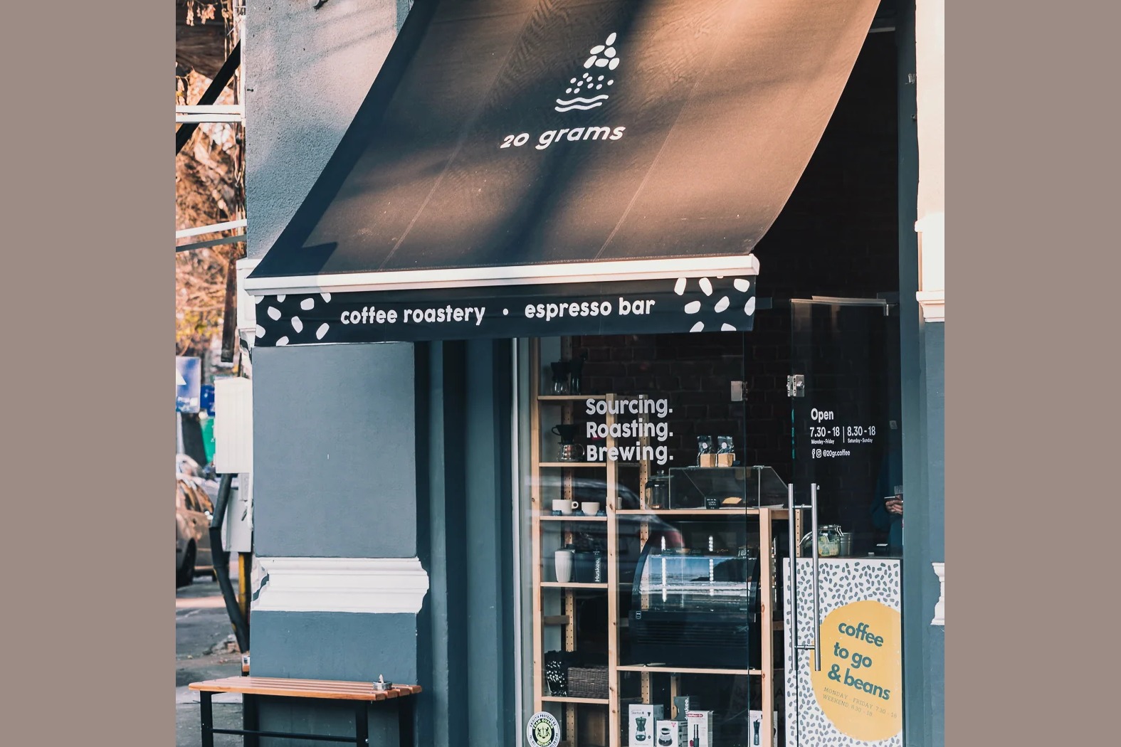 The 20 grams storefront with its coffee roastery and espresso bar awning, a Sourcing Roasting Brewing window display, and a bench out front
