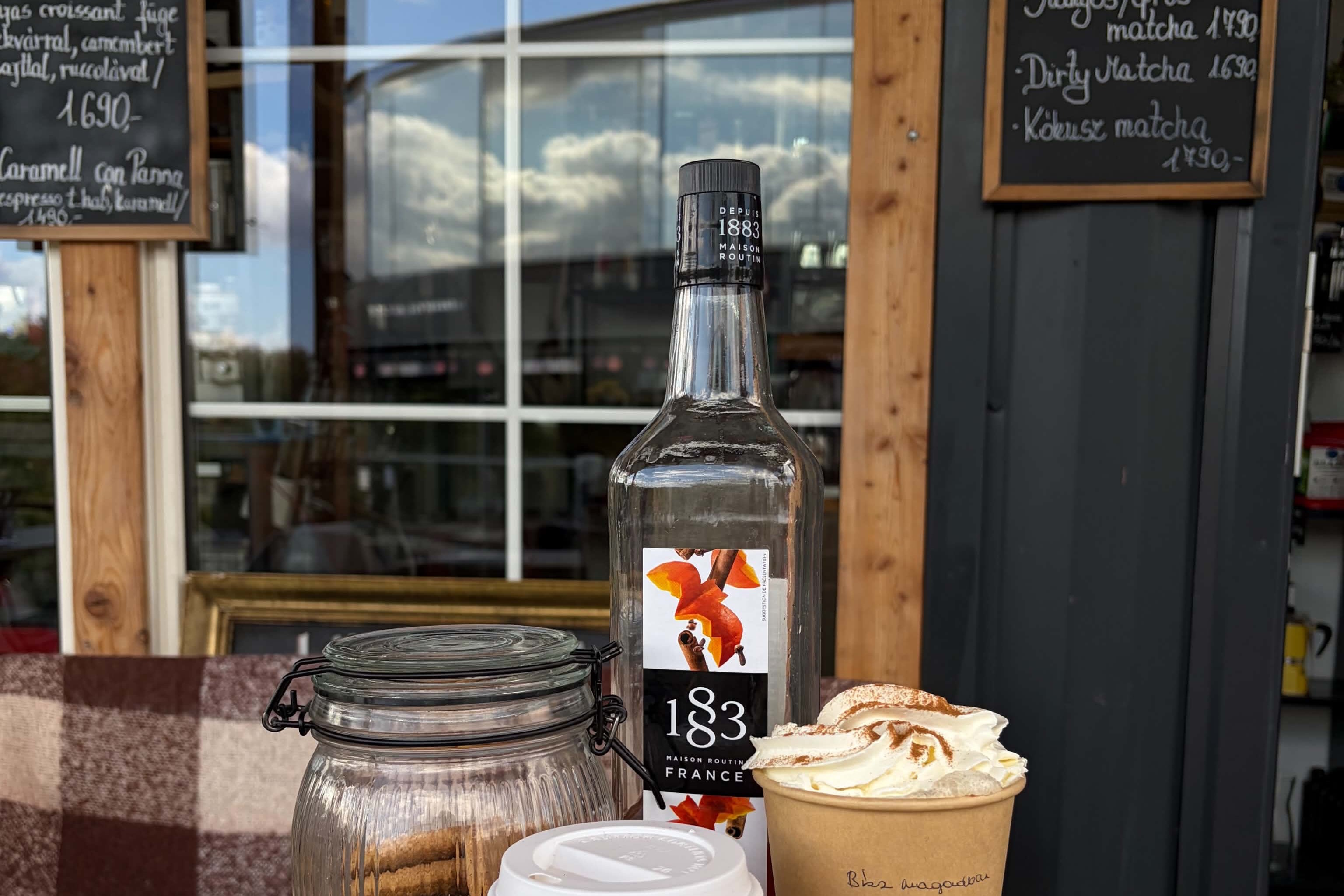 A table on Blue Monkey's terrace with cups and a syrup bottle, chalkboard menu boards and the storefront window with timber framing behind