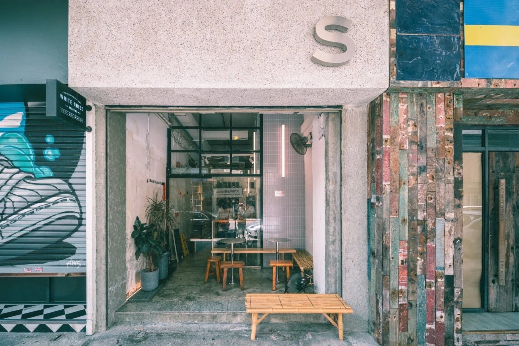 The open concrete storefront of Café Sausalito on Tai Nan Street with a steel S sign above, bamboo benches at the door and wooden stools inside