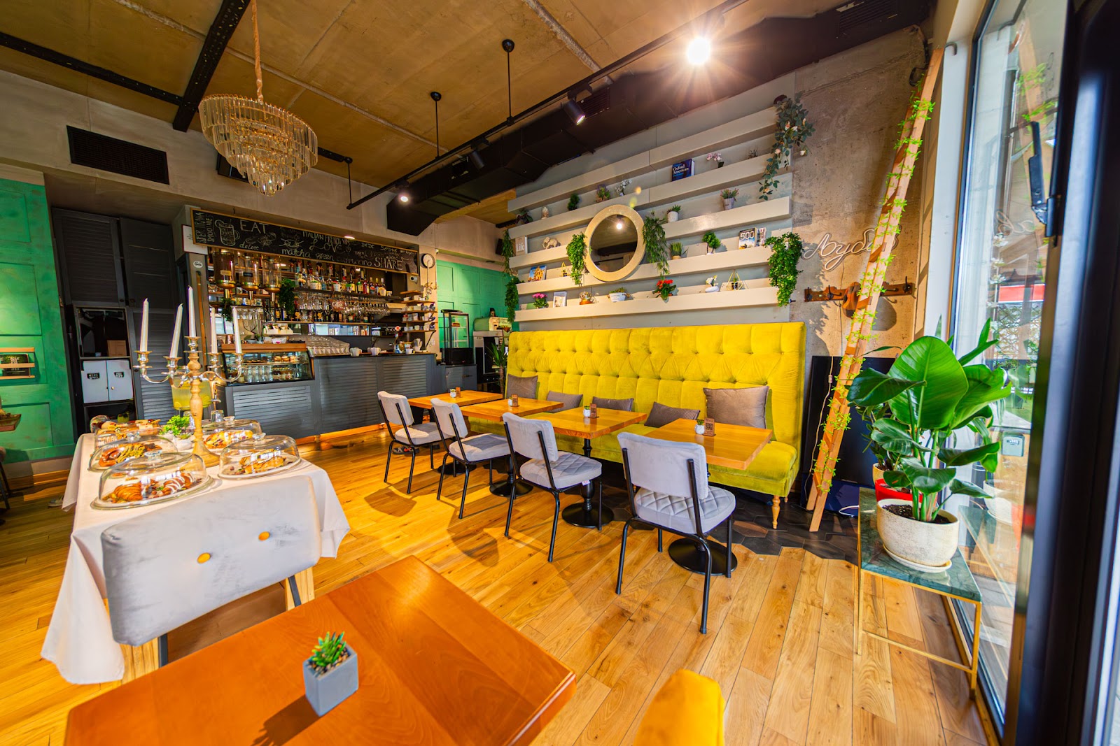 The plant filled interior of BRIEF coffee and brunch with yellow banquette seating and a chandelier